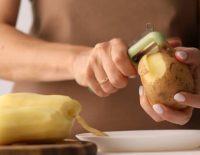 A young woman peels potatoes. Peeling raw vegetables. The process of food preparation.